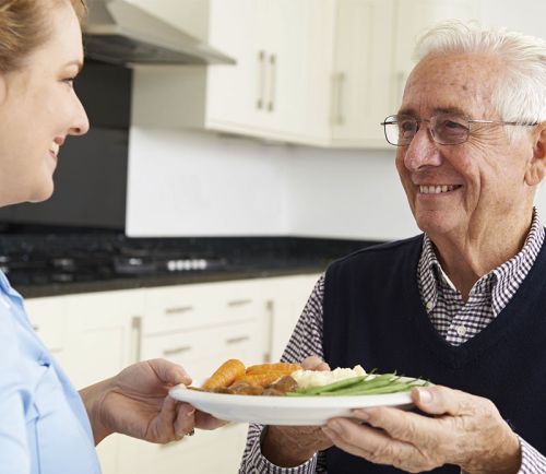 Pflegerin reicht Essen an älteren Herr
